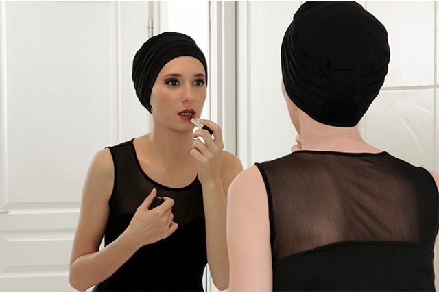 Photo d'une femme malade d'un cancer avec turbans en train de se maquiller devant une glace pour préserver son estime de soi